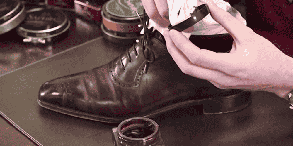 man cleaning brown leather shoes with cream shoe polish